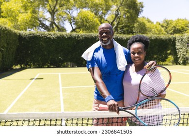 Portrait of happy senior african american couple with tennis rackets embracing on sunny grass court. Senior lifestyle, retirement, sport, summer, fitness, hobbies and leisure activities. - Powered by Shutterstock