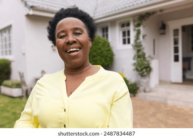 Portrait of happy senior african american woman wearing yellow shirt in garden at home. Domestic life, retirement, nature and lifestyle, unaltered. - Powered by Shutterstock