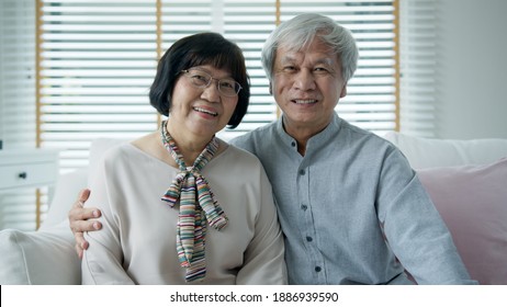 Portrait Of Happy Senior Asian Couple Relax Sitting Smile At Home Indoor On Sofa Couch Looking At Camera With Enjoy Retirement Or Quarantine Time. Attractive Asia Adult Older People Happy Lifestyle.