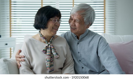 Portrait Of Happy Senior Asian Couple Relax Sitting Smile At Home Indoor On Sofa Couch Looking At Camera With Enjoy Retirement Or Quarantine Time. Attractive Asia Adult Older People Happy Lifestyle.