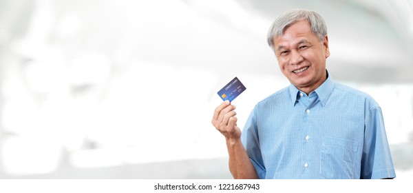 Portrait Of Happy Senior Asian Man Holding Credit Card And Showing On Hand Smiling And Looking At Camera On Isolated Blurred Background Banner Feeling Positive And Enjoy. Older Male Lifestyle Concept.