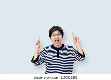 Portrait Of Happy Senior Asian Woman Gesture Or Pointing Hand And Finger Up And Looking At Camera On Isolated Background Feeling Positive And Enjoy. Older Female Lifestyle Concept With Clipping Path.