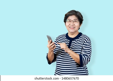 Portrait Of Happy Senior Asian Woman Holding Or Using Smartphone And Looking At Camera On Isolated Background Feeling Positive Enjoy And Satisfaction. Older Female Lifestyle Concept  Blue Background.