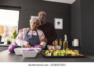 Portrait of happy senior biracial couple preparing vegetables and embracing in kitchen at home. Senior lifestyle, retirement, food, cooking and domestic life, unaltered. - Powered by Shutterstock