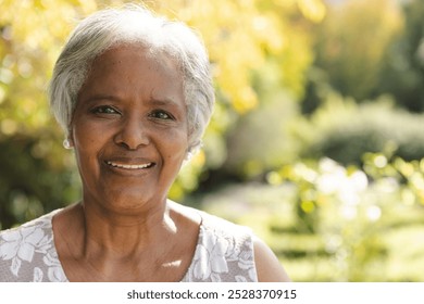 Portrait of happy senior biracial woman smiling in sunny garden at home, copy space. Happiness, nature, wellbeing, summer and senior lifestyle, unaltered. - Powered by Shutterstock