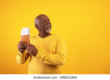 Portrait Of Happy Senior Black Man Holding Passport With Plane Boarding Pass Tickets, Looking Aside At Empty Space On Orange Studio Background. Overseas Tourism, Abroad Vacation Concept