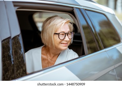 Portrait Of A Happy Senior Business Woman Looking Out The Car Window, Traveling On The Back Seat Of A Taxi