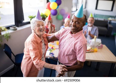 Portrait Of Happy Senior Couple Dancing By Table At Birthday Party