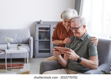 Portrait of happy senior couple using digital tablet together in minimal home interior, copy space - Powered by Shutterstock