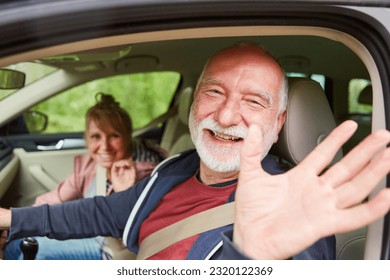 Portrait of happy senior couple waving while traveling in car during road trip at vacation - Powered by Shutterstock