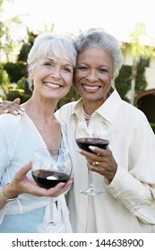 Portrait Of Happy Senior Female Friends Standing Outside With Wine Glasses