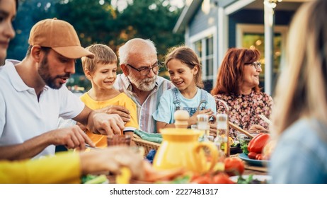 Portrait of a Happy Senior Grandfather Holding His Bright Talented Little Grandchildren on Lap at a Outdoors Dinner Party with Food and Drinks. Family Having a Picnic Together with Children. - Powered by Shutterstock