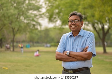 Portrait of a happy senior Indian man wearing a suit and hands crossed in the outside setting standing and thinking in a park in New Delhi, India