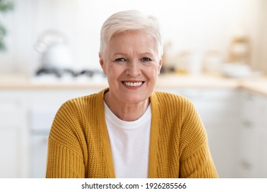 Portrait Of Happy Senior Lady Sitting In Kitchen At Home, Closeup, Copy Space. Attractive Old Woman With Grey Short Hair Smiling At Camera, Chilling After Cooking Dinner For Her Family