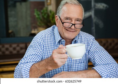 Portrait of happy senior man with coffee cup sitting at cafe