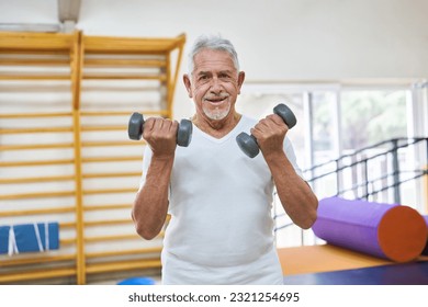 Portrait of happy senior man exercising with dumbbells at rehabilitation center - Powered by Shutterstock