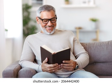 Portrait of happy senior man with grey hair in eyeglasses reading book at home, sitting on sofa in living room and smiling at camera, positive male pensioner enjoying life on retirement - Powered by Shutterstock