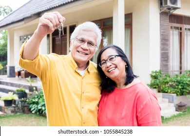 Portrait of a happy senior man posing with his wife while holding the keys of a residential house 