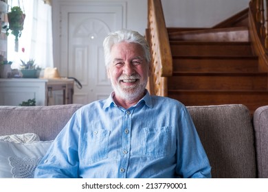 Portrait of happy senior man sitting on sofa in the living room of house in front of wooden staircase. Old male smiling while relaxing on couch and looking at camera - Powered by Shutterstock