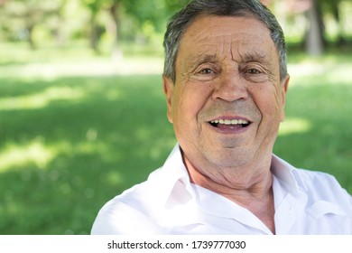 Portrait of happy senior man smiling, in the public park, outdoors.. Old man relaxing outdoors and looking at camera. Portrait of elderly man enjoying retirement