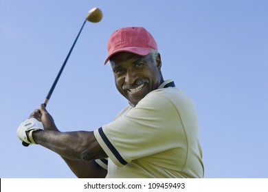 Portrait of a happy senior man swinging a golf club against clear sky