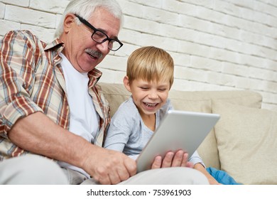 Portrait of happy senior man using digital tablet watching videos with grandson both laughing sitting on couch at home - Powered by Shutterstock