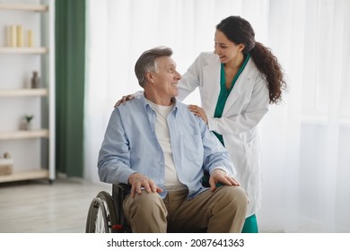 Portrait of happy senior man in wheelchair and his female nurse at retirement home. Mature male patient with disability and his caregiver posing and smiling, looking at each other indoors