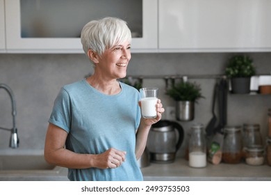 Portrait of a happy senior mature mid aged woman holding a glass and drinking milk and having a healthy breakfast after fitness exercise training in the morning at home - Powered by Shutterstock