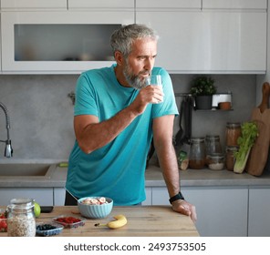 Portrait of a happy senior mature mid aged man holding a glass and drinking orange juice and having a healthy breakfast after fitness exercise training in the morning at home - Powered by Shutterstock