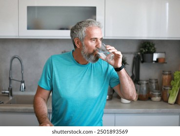 Portrait of a happy senior mature mid aged man holding a glass and drinking water and having a healthy breakfast after fitness exercise training in the morning at home - Powered by Shutterstock