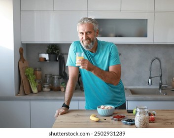 Portrait of a happy senior mature mid aged man holding a glass and drinking orange juice and having a healthy breakfast after fitness exercise training in the morning at home - Powered by Shutterstock