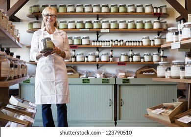 Portrait of a happy senior merchant standing with spice jar in store
