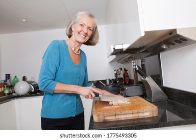 Portrait Of Happy Senior Woman Chopping Vegetables At Kitchen Counter