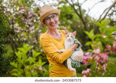 Portrait of happy senior woman holding her cute cat while gardening in yard. - Powered by Shutterstock