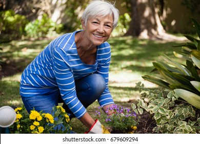 Portrait Of Happy Senior Woman Kneeling While Planting Flowers In Backyard