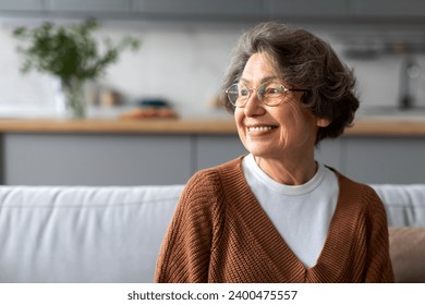 Portrait of happy senior woman relaxing on comfortable couch at home in living room and looking away at free space, enjoying domestic pastime - Powered by Shutterstock