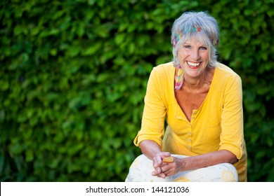 Portrait of happy senior woman sitting against creepers in park - Powered by Shutterstock