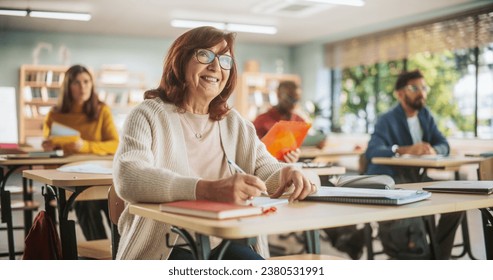 Portrait of a Happy Senior Woman Taking a Course in an International Adult Education Center. Focused Elderly Female Wearing Glasses, Sitting Behind a Desk, and Writing Down Notes in a Notebook. - Powered by Shutterstock