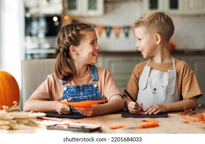 Portrait of happy siblings kids boy and girl making Halloween home decorations together while sitting at wooden table, brother and sister painting pumpkins and making paper cuttings - Powered by Shutterstock