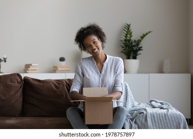 Portrait Of Happy Sincere Young African Multiracial Woman Sitting On Couch With Unwrapped Carton Parcel, Feeling Satisfied With Positive Online Shopping Experience, Distant Goods Purchasing Concept.