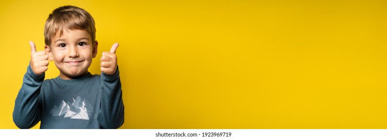 Portrait of happy small caucasian boy in front of yellow background thumbs up - Childhood growing up and achievement concept - front view waist up copy space - Shutterstock ID 1923969719