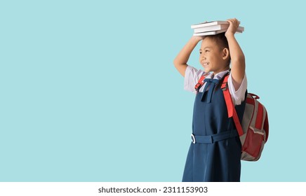 Portrait Happy smile asian school girl in uniform hold books on her head, back to school, carrying a school bag, isolated on pastel plain light blue background - Shutterstock ID 2311153903