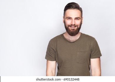 Portrait Of Happy Smiley Bearded Man With Dark Green T Shirt Against Light Gray Background. Studio Shot.  
