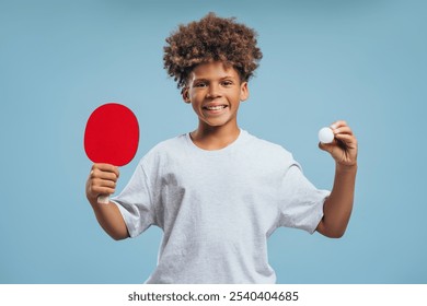 Portrait of happy, smiling African American boy with curly hair holding racket and tennis ball, looking at camera isolated on blue background. Ping pong game concept - Powered by Shutterstock