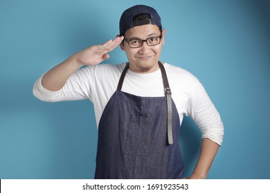 Portrait Of Happy Smiling Asian Chef Or Waiter Doing Salute Gesture, Ready To Serve, Against Blue Background