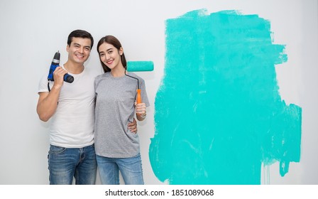 Portrait Of Happy Smiling Asian Couple Hand Holding Drill Renovating Painting Wall House. Mother Father Repairing Paint Wall At Home. Man And Woman Together Love Lifestyle Concept With Copy Space