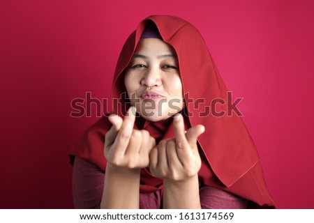 Portrait of happy smiling Asian muslim woman doing cash, rich,  money or love gesture, against red background
