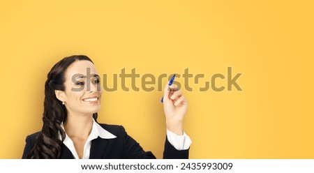 Portrait of happy smiling beautiful businesswoman wear black confident suit, writing or drawing something on screen, by marker. Brunette woman, isolated yellow studio wall background.