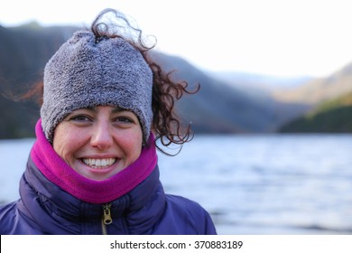 Portrait of a happy smiling beautiful woman wearing colorful warm winter clothes with a red face from the cold standing in mountain landscape in Ireland
