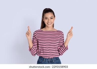 Portrait of happy smiling beautiful young woman with long brunette hair standing over grey studio background, holding fingers crossed for good luck and smiling at camera, copy space - Shutterstock ID 2293158903